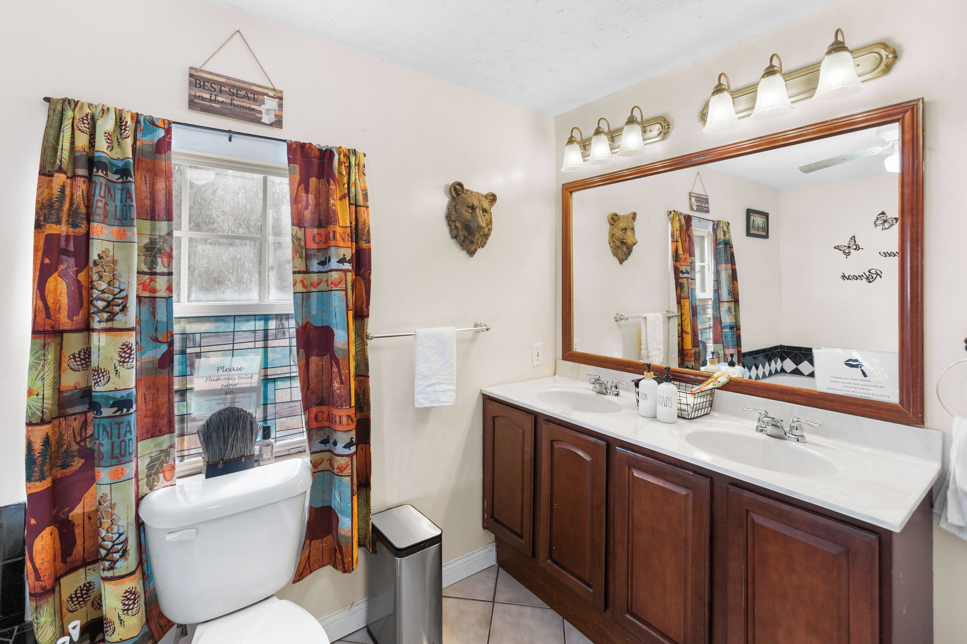 A bathroom with a large mirror, two sinks, a toilet, and a shower curtain with a forest print.