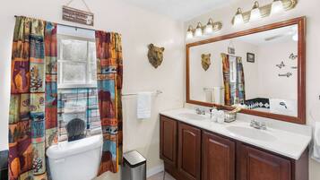 A bathroom with a large mirror, two sinks, a toilet, and a shower curtain with a forest print.