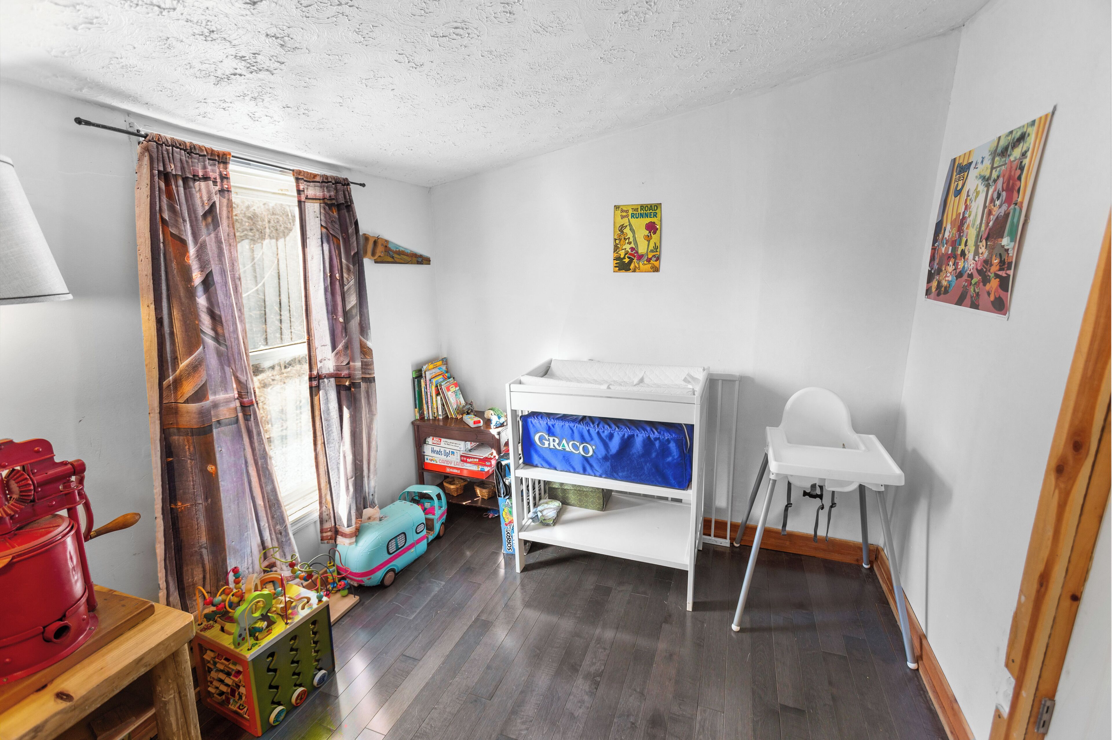 Een kinderkamer met een stapelbed, een klein bureau, een speelgoedauto en een kleurrijk poster aan de muur.