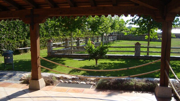A covered outdoor area with a stone floor, a rope barrier, and a view of a cemetery with trees and a fence. - Rural House La Casita (Ciudad Rodrigo)