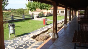 A covered patio with stone flooring, a wooden fence, and a grassy area with a stone planter. - Rural House La Casita (Ciudad Rodrigo)