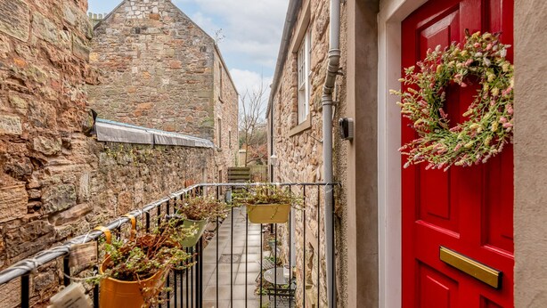 A narrow alleyway with stone buildings, a red door with a wreath, and hanging planters. - Little Haven | St Andrews Town Centre (St Andrews)