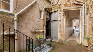 A narrow alleyway with a staircase, a small outdoor seating area with chairs and a table, and a door leading to a building. - Little Haven | St Andrews Town Centre (St Andrews)