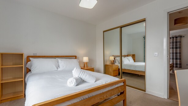 A bedroom with a wooden bed, a wardrobe with a mirror, and a bedside table with a lamp.