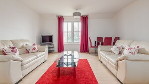A modern living room with two white leather sofas, a glass coffee table, and a red rug.