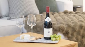 A cozy living room with a wooden coffee table, two wine glasses, a bottle of wine, a cheese platter, and a blanket. - True Luxury - Pool, HT, Sauna (Whistler)