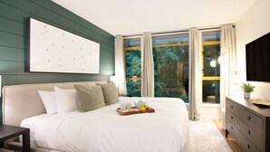 A bedroom with a large bed, a bedside table, a dresser, a TV, and a window with curtains. - True Luxury - Pool, HT, Sauna (Whistler)