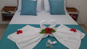 A hotel room with a bed, two pillows, a nightstand, and a towel arrangement on the bed. - Pousada Conchas Do Mar (Cairu)