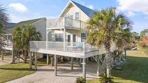 A two-story house with a balcony, surrounded by palm trees and a grassy yard.