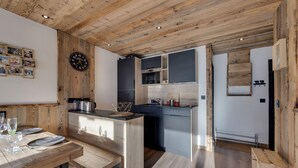 A modern kitchen with wooden ceiling beams, a central island, and a dining area with a wooden table and chairs. - Beautiful renovated apartment (Val-d'Isère)