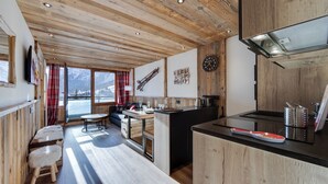 A modern kitchen with wooden beams, a large window with a view of mountains, and a dining area with a bench. - Beautiful renovated apartment (Val-d'Isère)