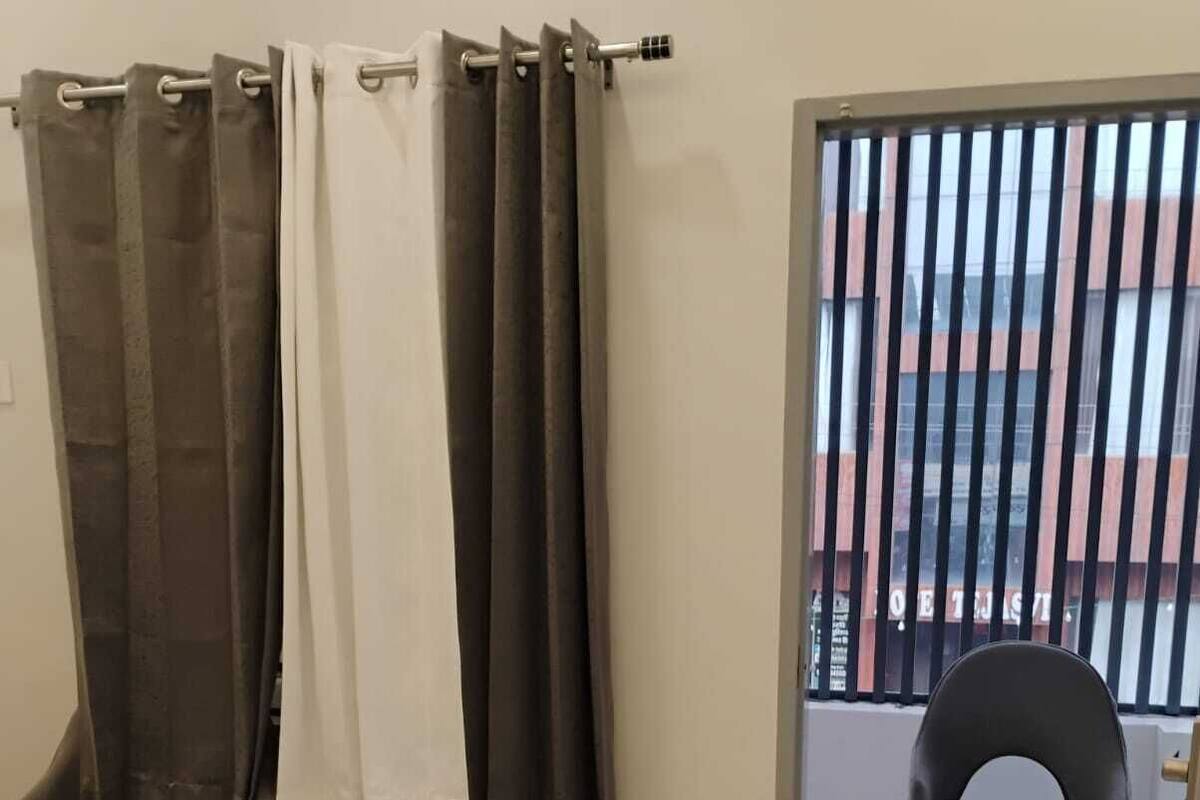 A hotel room with a bed, a chair, and a view of a building through a window with a metal railing.