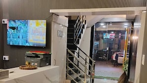 A modern reception area with a marble counter, a television mounted on the wall, and a staircase leading to an upper floor. - Aastha Guest House (Roorkee)