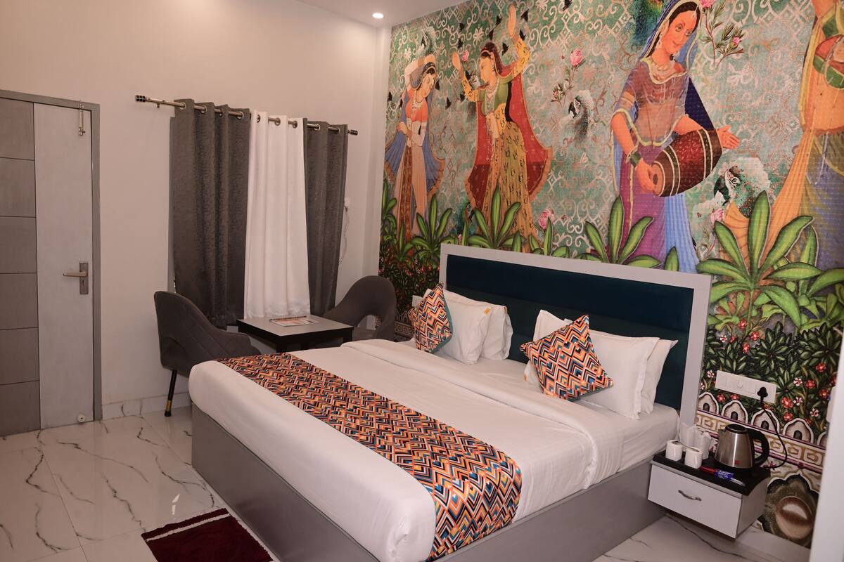 A hotel room with a bed, a desk, a chair, a nightstand, and a mural on the wall.