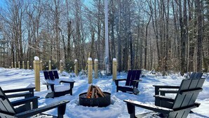 A snow-covered outdoor seating area with Adirondack chairs and a fire pit.