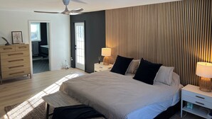 A bedroom with a bed, bedside tables, a ceiling fan, a window, and a door leading to a bathroom.