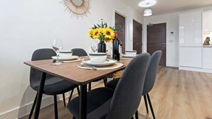 Un coin repas avec une table en bois, des chaises noires, des assiettes blanches et un vase rempli de tournesols.