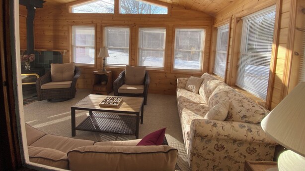 A cozy wooden cabin interior with a high ceiling, large windows, a sofa, a coffee table, and a fireplace. - Newly furnished ranch style home within 5 miles of Gore Mtn Ski Center (North Creek)