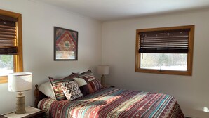 A bedroom with a bed, a nightstand, a lamp, a wall art piece, and a window with blinds. - Newly furnished ranch style home within 5 miles of Gore Mtn Ski Center (North Creek)