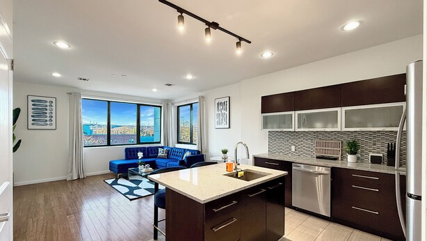A modern kitchen with a central island, dark cabinetry, and a view through large windows. - Luxe 2BR Master Suite Near NYC (East Orange)