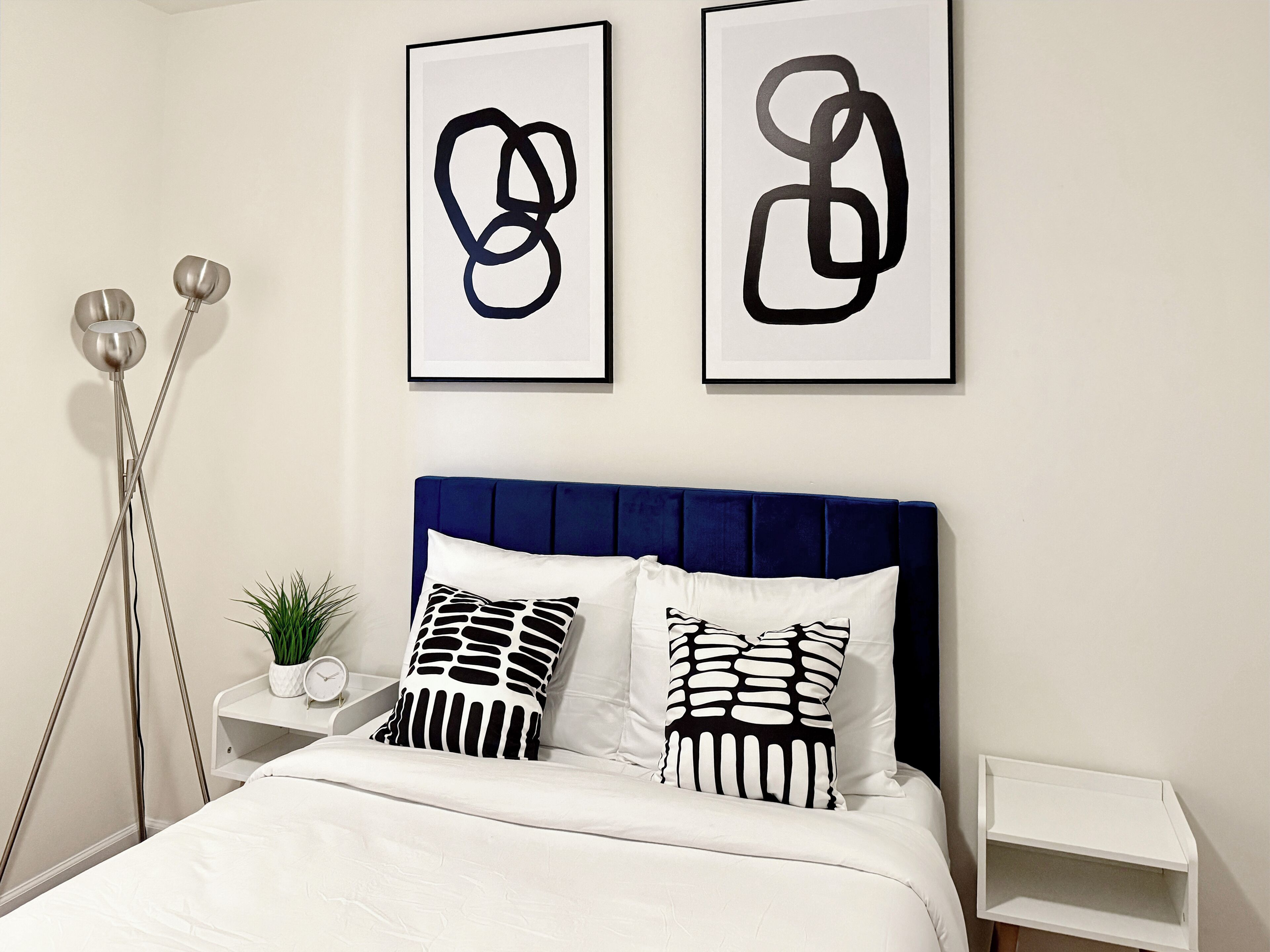 Una camera da letto con una testiera blu, biancheria da letto bianca e due opere d'arte astratte alle pareti.