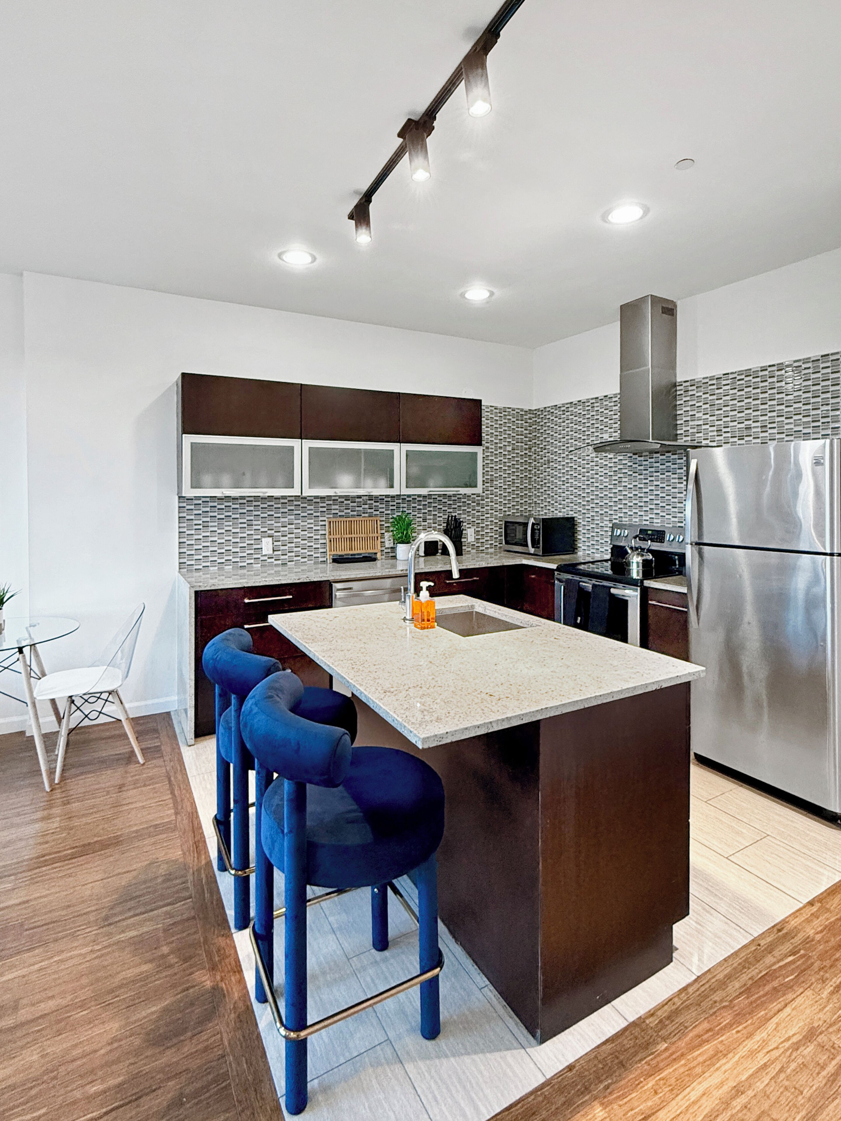 A modern kitchen with a central island, bar stools, a stainless steel refrigerator, and a microwave.