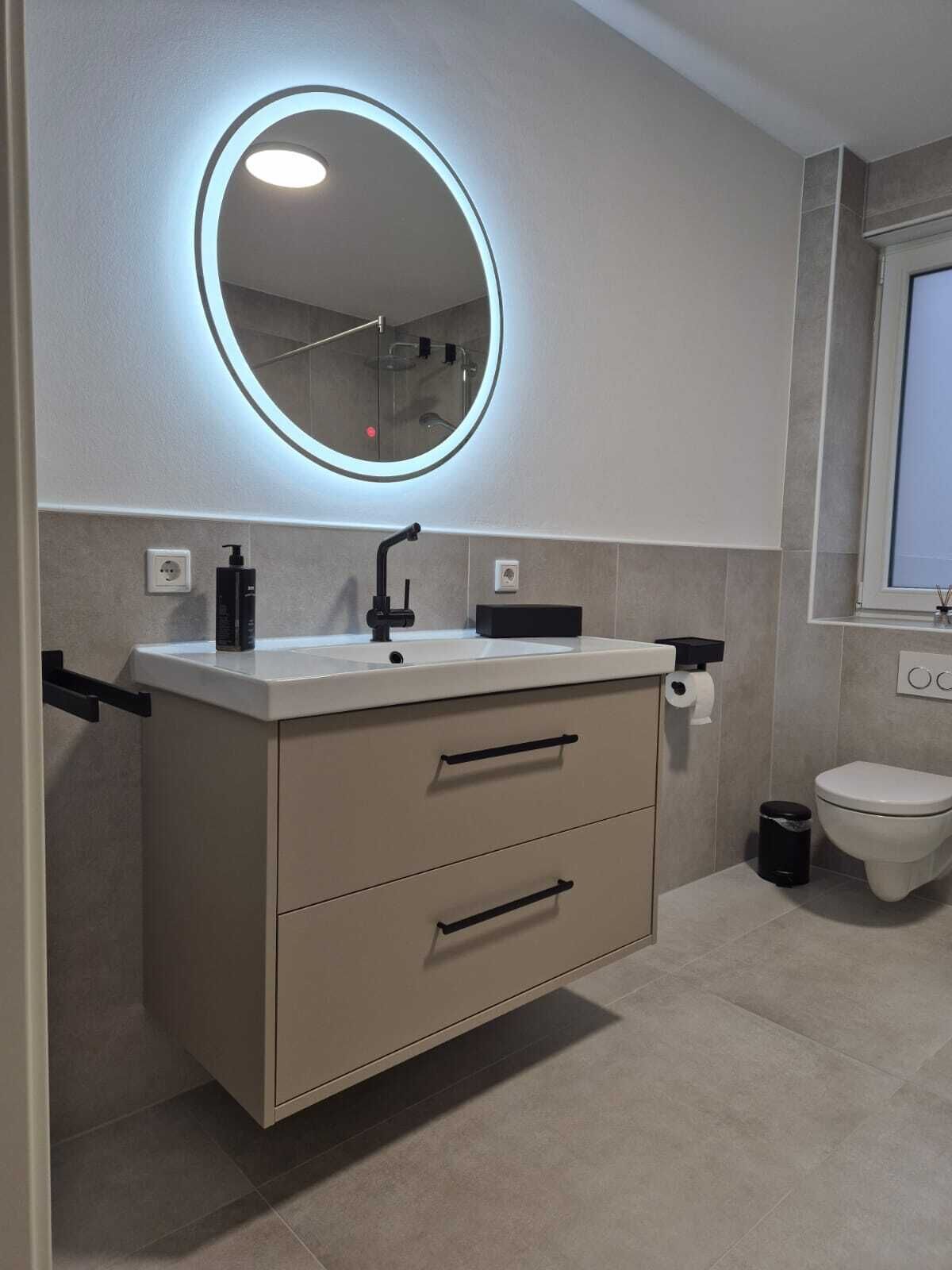 Ein modernes Badezimmer mit rundem Spiegel, Waschbecken und Toilette.