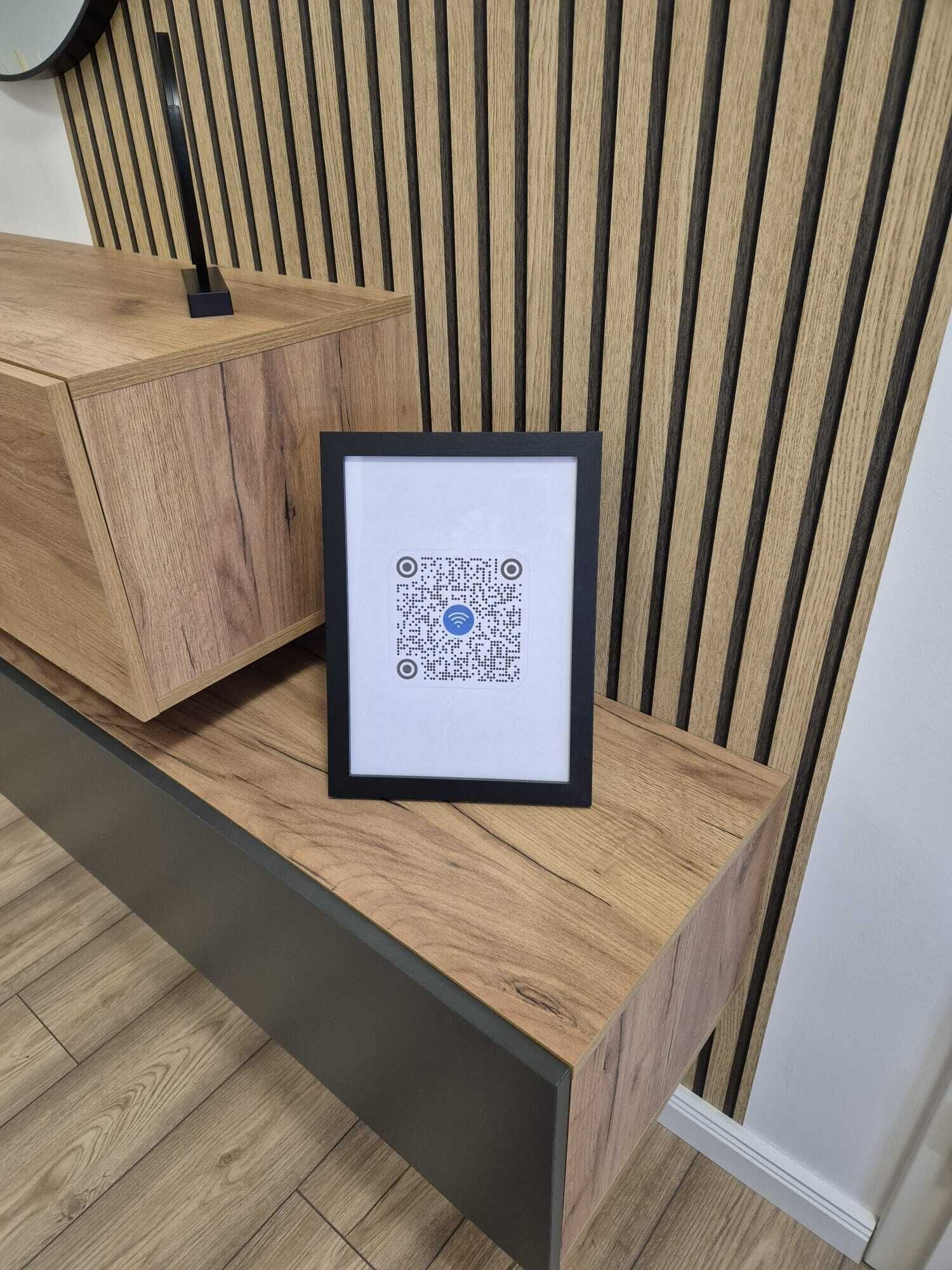 En inramad QR-kod på ett skrivbord i trä, med en vägg i bakgrunden som har vertikala ränder.