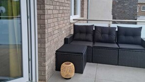 Un área de estar moderna al aire libre con un sofá y una mesita, una cesta de mimbre y un ventanal que da a un balcón.