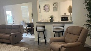 A living room with a beige sofa, two bar stools, and a kitchen area with a counter and decorative items. - Charming 4-bedroom house with WiFi and AC in wonderful Spring (Spring)