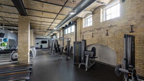 Un gimnasio con diversos equipos de ejercicio, una pared de ladrillo y ventanas amplias.
