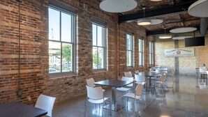 Un espacio interior amplio con paredes de ladrillo, ventanas grandes y varias mesas y sillas.