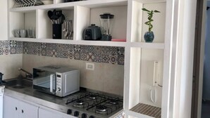 A kitchen with a gas stove, a toaster, a coffee maker, and a blender on the countertop. There are shelves above holding dishes, cups, and a plant.