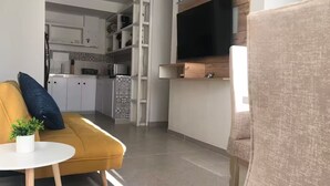 A modern living room with a yellow sofa, a small round table with a plant, and a TV mounted on the wall.