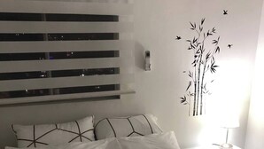 A neatly made bed with patterned bedding, a wall-mounted thermostat, and a wall decoration of bamboo and birds.