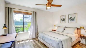 A bedroom with a bed, desk, chair, ceiling fan, and two framed pictures on the wall.