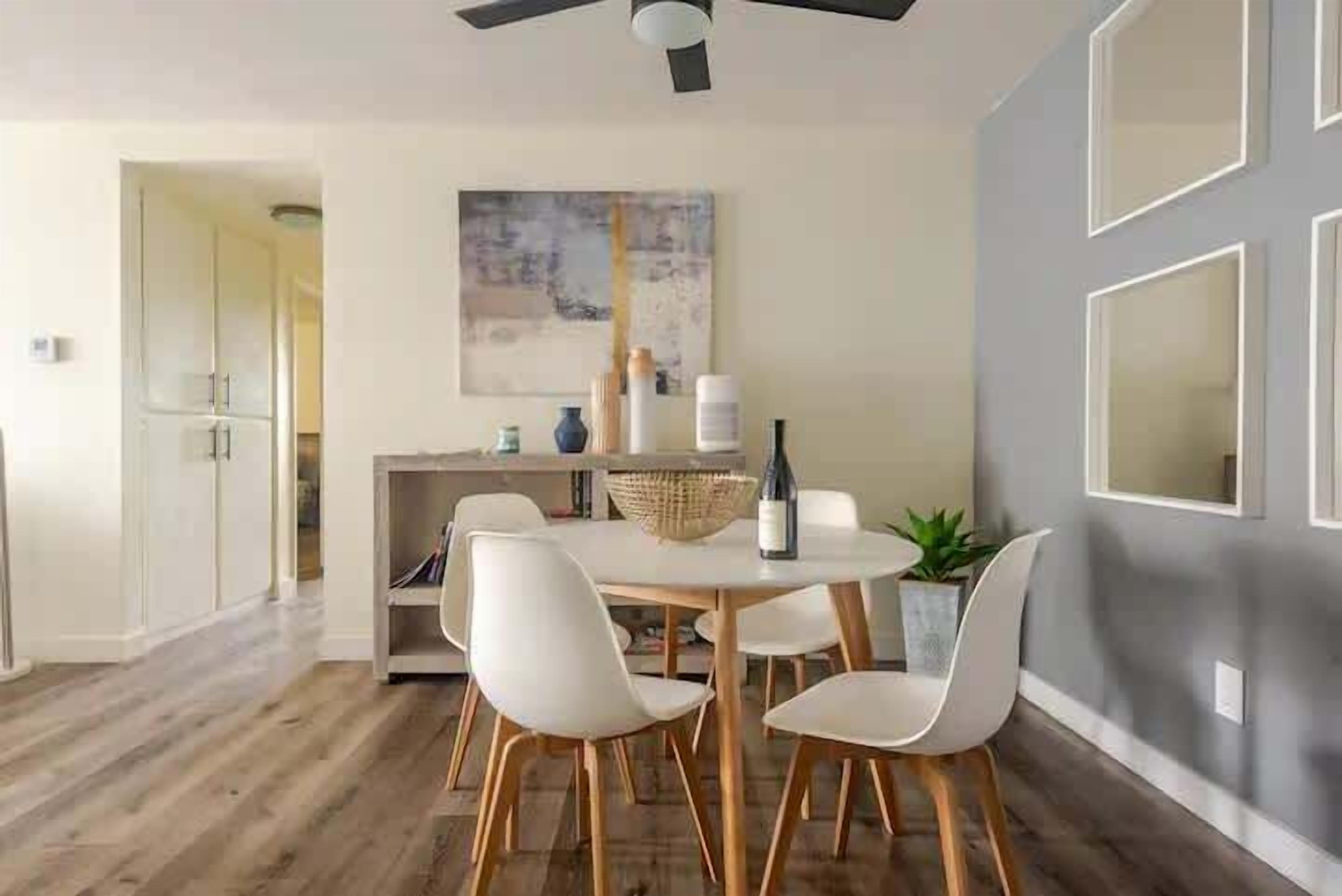 A dining area with a round table, white chairs, and a ceiling fan.