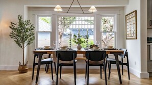 A dining area with a wooden table set for four, two black chairs, a potted plant, and a window with a view of a house. - Balboa Park, Zoo, Downtown! BRAND NEW (San Diego)