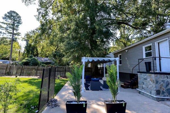 Un jardin avec un patio couvert, un mur en pierre et une clôture en bois.