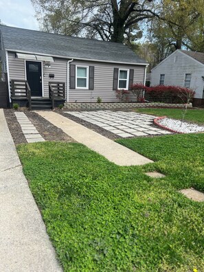 A residential house with a front yard, a pathway leading to the front door, and a small garden area.