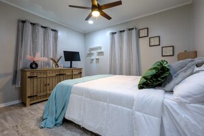 Une chambre à coucher avec un lit, une commode en bois, un ventilateur de plafond et des rideaux légers.