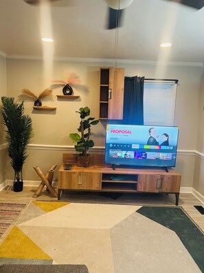 Ein Wohnzimmer mit einem Flachbildfernseher, der einen Film zeigt, einer Holz-Unterhaltungsanlage, einem Topfpflanzen und einem dekorativen Wandschrank.