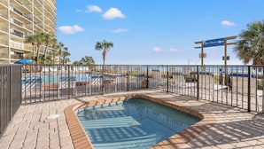 A hotel pool area with a clear view of the pool, palm trees, and a building in the background.