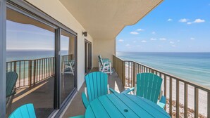 A balcony with a view of the ocean, turquoise chairs, and a table.