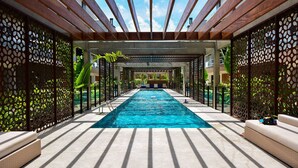 A long swimming pool with a wooden pergola overhead, surrounded by decorative screens and outdoor seating. - SunClub - 300 metros da Praia do Campeche - SDI014 (Florianópolis)