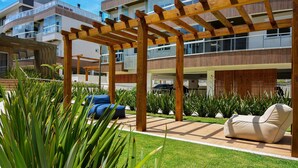 A modern outdoor area with a wooden pergola, a beige lounge chair, and a blue sofa. - SunClub - 300 metros da Praia do Campeche - SDI014 (Florianópolis)
