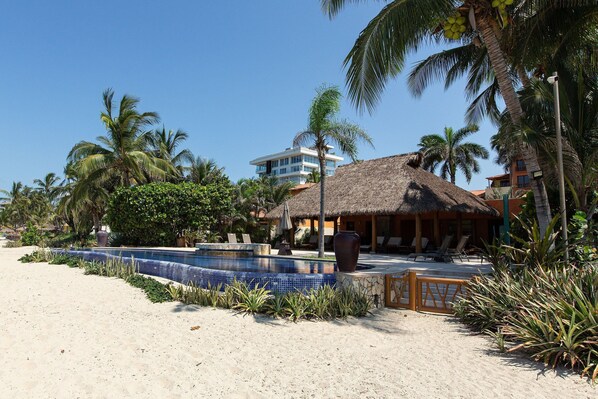 Un resort con piscina, playa y edificio de techo de paja.