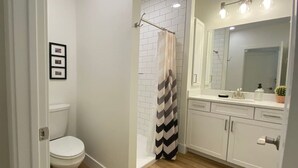A modern bathroom with a white toilet, a shower with a striped curtain, and a vanity with a mirror and lights.