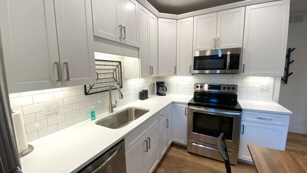 A modern kitchen with white cabinets, stainless steel appliances, and a wooden dining table.