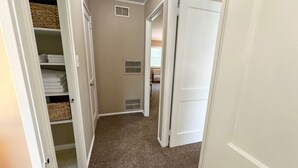 A narrow hallway with white doors, a carpeted floor, and a closet with folded towels and baskets. - Cute and Cozy Near Parks (Midland)